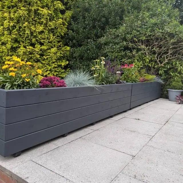 Long bespoke grey wooden planter filled with garden plants on a patio